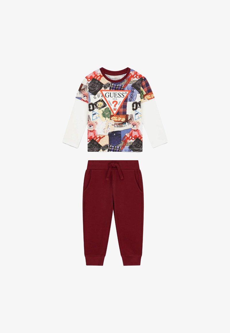 Le haut à manches longues présente un imprimé graphique coloré avec des motifs variés et le logo "Guess" ; le pantalon de survêtement rouge possède une taille élastique et des poches.