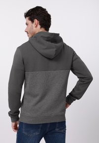 Hanorac gri cu un design texturat în jumătatea inferioară, cu glugă și mansete striate, asortat cu blugi albaștri.