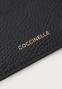 Portafoglio in pelle nera con texture, caratterizzato da un logo dorato in rilievo "COCCINELLE" sulla parte anteriore, design minimalista con cuciture ordinate.