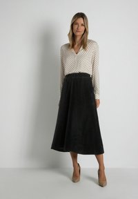 Romantische crème blouse met zwarte stippen en V-hals. Zwarte corduroy midi rok met een gladde textuur. Beige hoge hakken maken de outfit compleet.