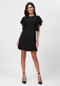 Robe noire avec des manches courtes volantées, corsage ajusté et jupe évasée. Tissu lisse de couleur unie et longueur au-dessus du genou.