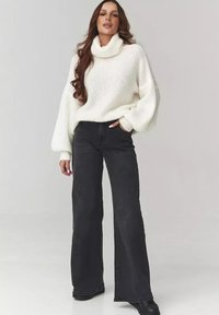 Biały sweter z dzianiny z wysokim kołnierzem i szerokimi rękawami, zestawiony z czarnymi, szerokimi spodniami z wysokim stanem, prezentującymi luźną sylwetkę.