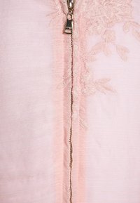 Różowa odzież z zamkiem błyskawicznym, zdobiona haftem kwiatowym wokół zamka. Materiał jest lekki i ma lekko teksturowane wykończenie.