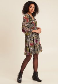Blumenkleid in Schwarz, Grün, Pink und Rot mit langen Ärmeln, geraffter Taille und geschichteter Saum. Kombiniert mit schwarzen Knöchelstiefeln.