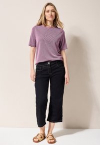 Top rosa a maniche corte, pantaloni capri in denim scuro con cuciture a contrasto e sandali intrecciati color sabbia, su sfondo neutro.