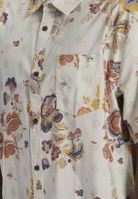 Kevyt kangas, jossa lyhythihainen paita ja kukkakuosi. Kuvioissa on sinistä, keltaista ja pinkkiä, ja siinä on ruskeat napit sekä rintatasku.