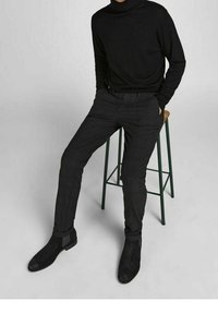 Black turtleneck sweater and tailored pants worn with ankle boots. The materials appear smooth with a sleek, fitted design.