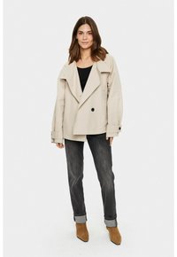 Beige oversize dvouřadový kabát, široké klopy, velké knoflíky, s ohrnutými rukávy. V kombinaci s černým topem a tmavými džíny, hnědými kotníkovými botami.