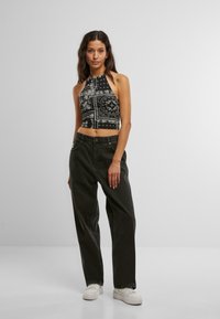 Mustvalge mustriga kaelusest crop top, mis on paaritatud tumedate lahtiste teksade ja valgete tennisetossudega. Mudel seisab ühtlase halli tausta ees.