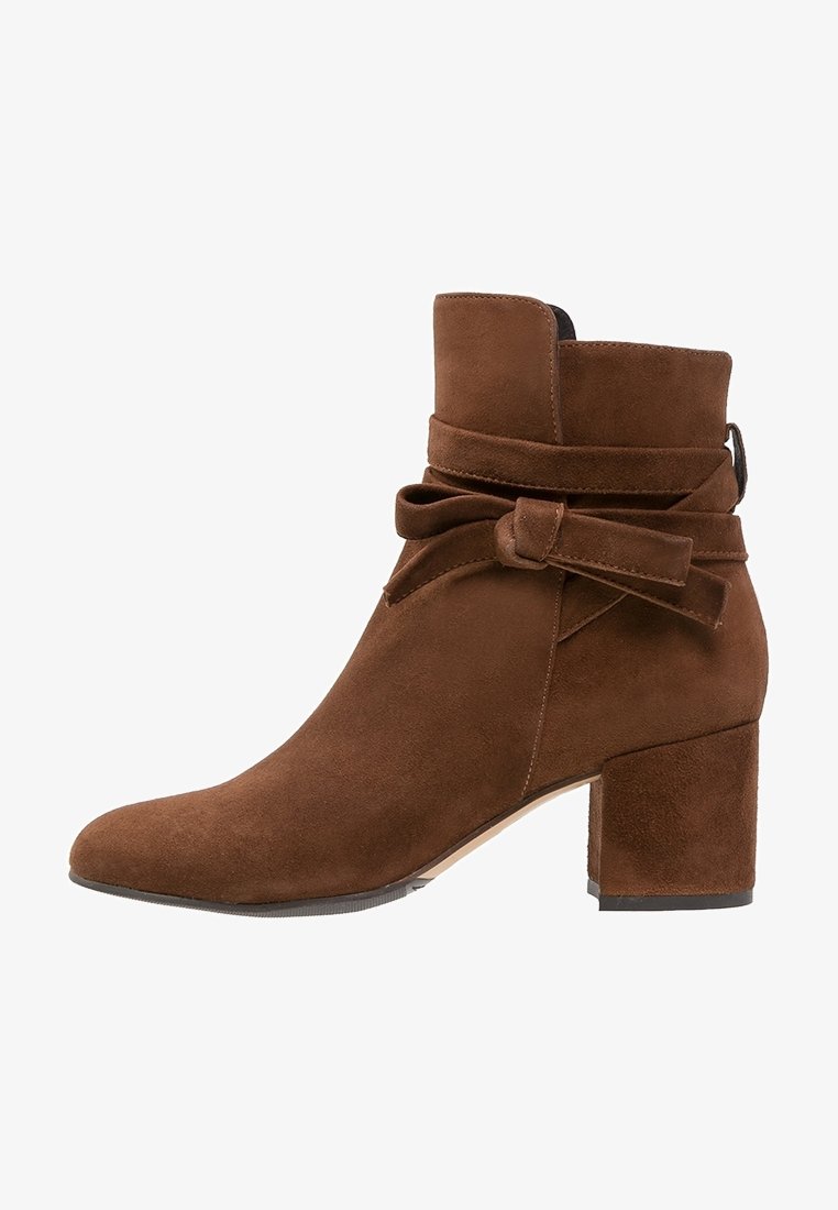 Bottine en daim marron avec talon carré et détail nœud entourant le côté.