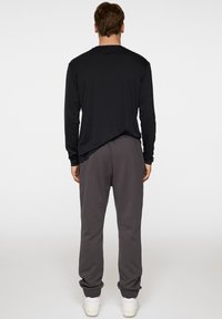 Czarna koszulka z długim rękawem i szare dresy, wykonane z miękkiego materiału, w luźnym kroju. Spodnie mają ściągacze na kostkach. Pod spodem białe sneakersy.