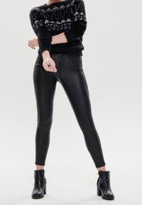 Svarta fusk läderbyxor med smal passform och texturerade paneler, tillsammans med en fluffig svart och vit mönstrad tröja och svarta ankelstövlar.