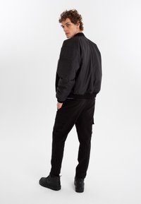 Black bomber jacket with ribbed cuffs, textured fabric, and side pockets, paired with black cargo pants and black sneakers.