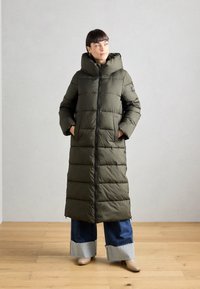Pohodlný dlhý kabát v olivovej farbe s vysokým golierom a zipsom. Má postranné vrecká a výrazné horizontálne prešívanie.