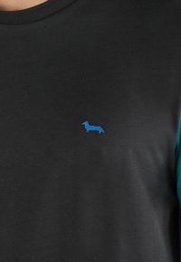 Sort bomulds-skjorte med et lille blå broderet dachshund-design på brystet og kontrastfarvet teal-stof på ærmerne.