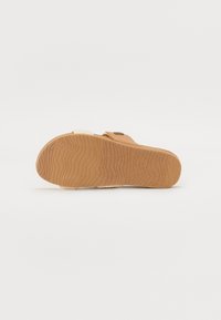 Světlé hnědé sandálové podešve s texturovaným gumovým povrchem. Obsahuje tkaný látkový pásek s akcentem z tanové spony. Plochý a minimalistický design.