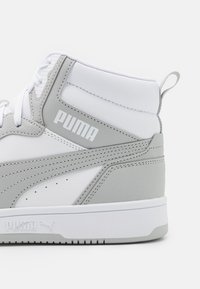 Baskets montantes en cuir synthétique blanc et gris clair avec des accents texturés et un logo "PUMA" blanc bien en vue sur le côté.