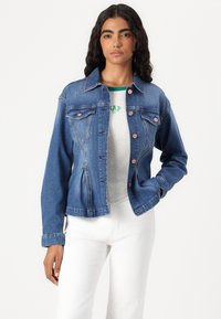 Light blue denim jacket with a fitted design, featuring front pockets, copper buttons, and a button-up closure. Worn over a gray shirt.