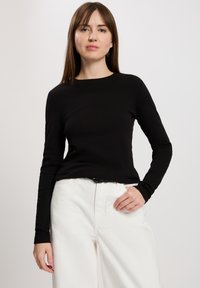 Czarny top z długim rękawem i okrągłym dekoltem, noszony z białymi spodniami o szerokich nogawkach. Tkanina ma gładką teksturę i dopasowany krój.