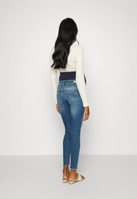 Smal jeans i ljusblå denim med hög midja. Långärmad krämfärgad topp, beige sandaler. Litet fransat nederkant vid ankeln.