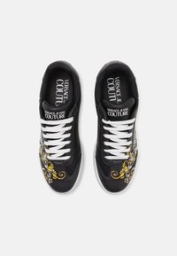 Czarne syntetyczne sneakersy z białymi sznurowadłami, złożone z misternych żółtych i białych haftów kwiatowych po bokach. Logo wydrukowane wewnątrz.