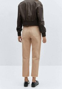 Veste courte en cuir marron avec poignets côtelés, associée à un jean beige clair à jambes droites et des mocassins noirs, vue de dos.