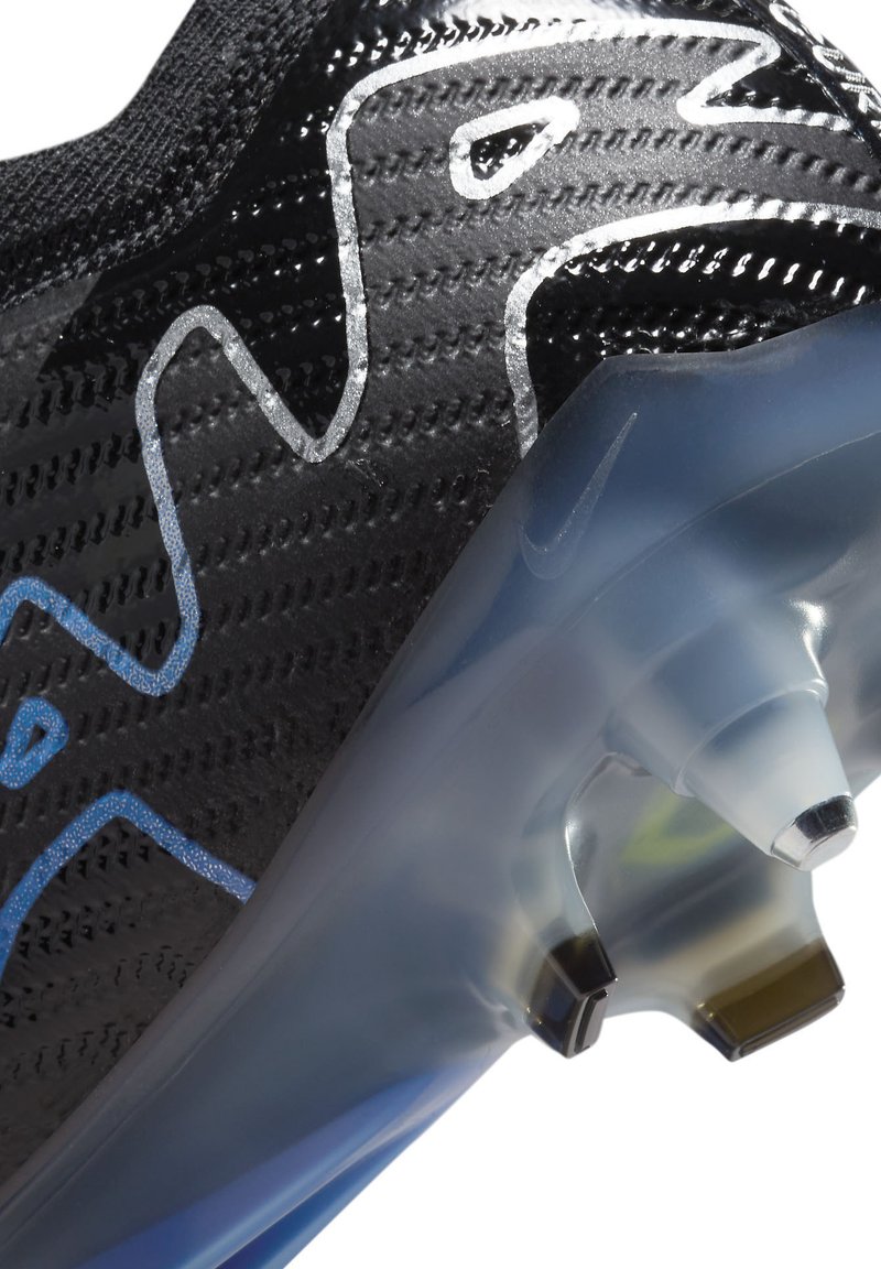 Scarpa sportiva nera con superficie strutturata, caratterizzata da un accento blu e una suola traslucida con tacchetti visibili per la trazione.