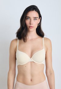 Beige gewatteerde bh met verstelbare bandjes, gladde textuur en een naadloos ontwerp. Kenmerkt zich door een centrale rimpeling voor subtiele vormgeving.