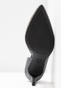 Chaussure à bout pointu avec une tige en tissu gris texturé, un talon fin noir et une semelle extérieure en caoutchouc ornée d'un motif de logo.