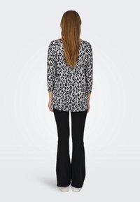 Top leopard stampato in bianco e nero con maniche a tre quarti, fessure laterali e orlo arrotondato, abbinato a pantaloni neri svasati e sneaker bianche.