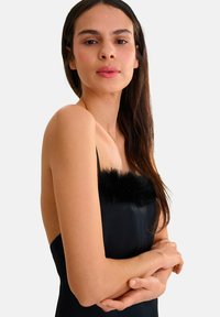 Robe noire avec un doux et moelleux bord noir le long du décolleté, ornée de fines bretelles et d'une silhouette ajustée.