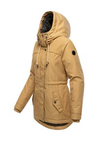 Tan parkas med pelsforet hette, snøring og trykknapper. Har sidelommer og ribbestrikkede mansjetter for varme.
