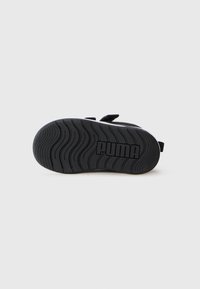 Semelle de sandale Puma noire avec un motif de semelle ondulée et des sangles en Velcro visibles sur fond blanc.