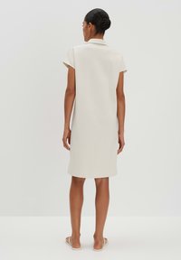Beiges kurzärmliges Kleid mit Kragen, gerade geschnitten und knielang. Glatte Textur und minimalistisches Design.