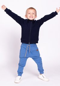 Granatowa bluza z zamkiem i wysokim kołnierzem, zestawiona z niebieskimi dresami z troczkami, o teksturowanym wykończeniu i boczną kieszenią. Całość dopełniają białe trampki.