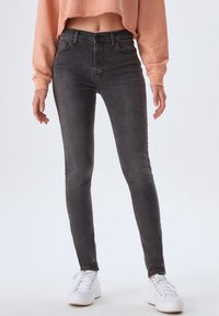 Jean skinny gris taille haute, présentant une texture en denim lisse et un design minimaliste, associés à des baskets blanches et un sweat-shirt court pêche.