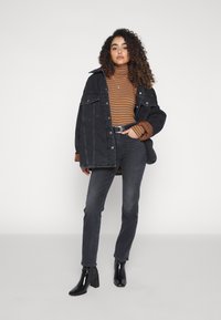 Giacca in denim nero con vestibilità oversize, maniche color ruggine, dolcevita a righe, jeans scuri e stivali neri lucidi con tacco.