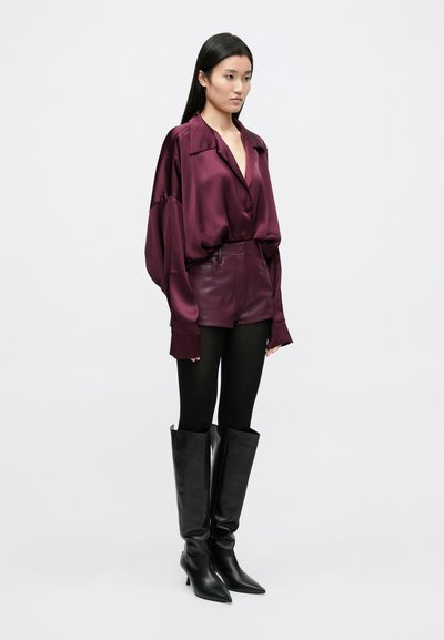 Burgundijos spalvos atlasinė palaidinė su didelėmis rankovėmis, aptempti odiniai šortai, juodos pėdkelnės ir odiniai ilgaauliai batai su smailiomis nosimis.