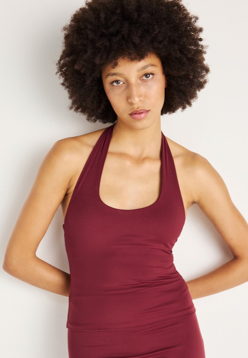 Top halter bordeaux feito de tecido elástico, com um decote redondo e design ajustado. Textura suave com costuras mínimas para maior conforto.