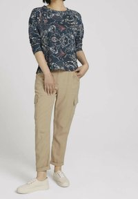 Maglietta a maniche lunghe blu navy con stampa floreale, abbinata a pantaloni cargo beige e sneakers di colore chiaro, con polsini arrotolati e tasche laterali.