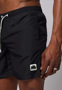 Pantaloni da nuoto neri realizzati in materiale leggero, con una vita elasticizzata, cordino e un patch con logo bianco sul lato sinistro in basso.