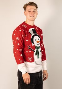Red Christmas sweater featuring a large snowman graphic with a black hat, green scarf, and white snowflakes. Ribbed white cuffs and hem.