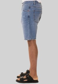 Shorts di jeans azzurri chiari con un taglio classico, dotati di tasca posteriore e orlo sfrangiato, abbinati a sandali neri con cinturini regolabili.