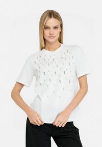 T-shirt bianco a maniche corte condecorazioni distribuite di perle e strass, colletto rotondo e vestibilità rilassata.