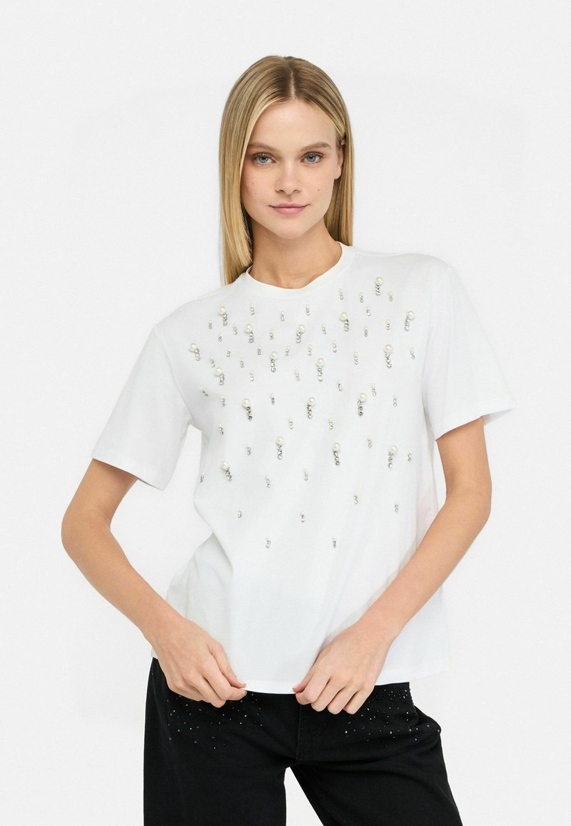 T-shirt bianco a maniche corte condecorazioni distribuite di perle e strass, colletto rotondo e vestibilità rilassata.