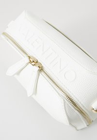 Balta teksturēta ādas soma ar zelta rāvējslēdzēju un iespiestu "VALENTINO" logotipu. Izstrādāta ar diviem rāvējslēdzēja vilkšanas mehānismiem un niansētām akcentiem.