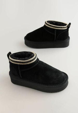 Bottines en suede noir avec une doublure en fausse fourrure et un poignet décoratif rehaussé de doré. Semelle en caoutchouc noir épaisse.