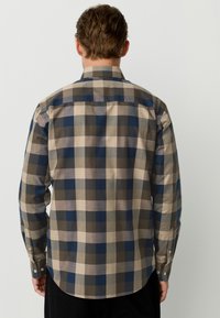 Long-sleeve plaid shirt in shades of beige, brown, and navy. Features a collared neck and button cuffs. Smooth, woven fabric texture.