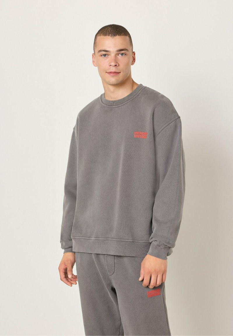 Hall hõbedane dressipluus tekstureeritud kangast, ümar kaelus, millel on rinnal tikandina punane logo. Looduslik lõige ja soonikkoes mansetid.