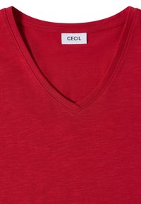 T-shirt rouge col en V avec une étiquette blanche cousue indiquant le nom de la marque Cecil à l'arrière du col intérieur.